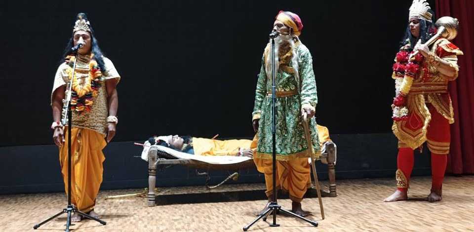 Artists of the Dhai Kadi Ki Ramleela in costume on stage, each delivering their own lines at a standing microphone